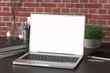 © dimamoroz - Workspace with blank laptop monitor white screen mock up on the dark desk near red brick wall. 3d illustration