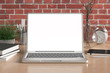© dimamoroz - Workspace with blank laptop monitor white screen mock up on the wooden desk near red brick wall. 3d illustration