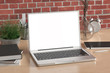 © dimamoroz - Workspace with blank laptop monitor white screen mock up on the wooden desk near red brick wall. 3d illustration