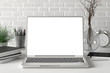 © dimamoroz - Workspace with blank laptop monitor white screen mock up on the white desk near white brick wall. 3d illustration