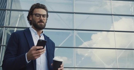 Handsome bearded Startup Businessman in Glasses using mobile Phone. Young man texting Messages, cheating on his Smartphone while walking in Office District. Business. Social Networking. People. Apps.