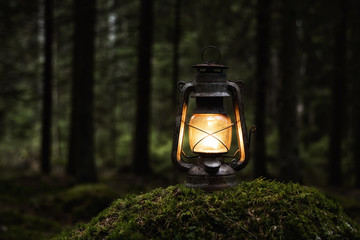 old kerosene lamp on the moss in mysterious dark forest. vintage lantern lighting. copy space.