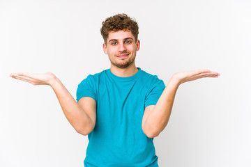 Young blond curly hair caucasian man isolated makes scale with arms, feels happy and confident.