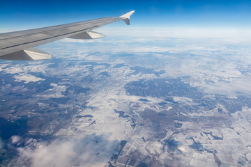 Plane silver wing during a flight over white clouds and a winter land is on the photo