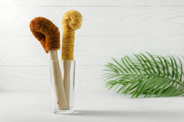 Two scrapers made of coconut bristles and a bamboo handle in a glass cup. Biodegradable kitchen accessories for washing dishes and zero waste concept. Image contains copy space.