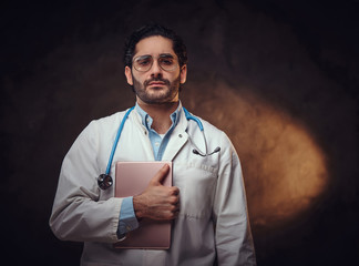 Wall Mural - Portrait of tired medic intern with tablet in his hands over dark background.