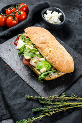 Ciabatta sandwich with fresh goat cheese, pear marmalade and arugula. Black background. Top view