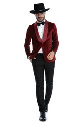 elegant fashion man in red velvet tuxedo wearing hat and walking