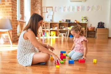 Poster - Beautiful teacher and blond toddler girl building tower using plastic blocks at kindergarten