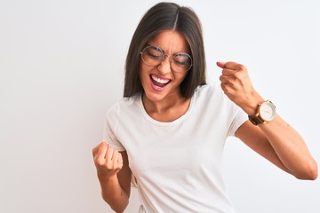 Wall Mural - Young beautiful woman wearing casual t-shirt and glasses over isolated white background very happy and excited doing winner gesture with arms raised, smiling and screaming for success. Celebration