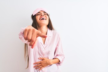 Poster - Young beautiful woman wearing sleep mask and pajama over isolated white background laughing at you, pointing finger to the camera with hand over body, shame expression