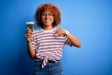 Young Beautiful African American Afro Woman With Curly Hair On Vacation Drinking Glass Of Beer With Surprise Face Pointing Finger To Himself