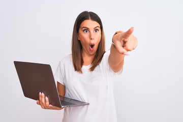 Wall Mural - Beautiful young woman working using computer laptop over white background Pointing with finger surprised ahead, open mouth amazed expression, something on the front