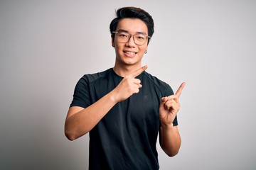 Young handsome chinese man wearing black t-shirt and glasses over white background smiling and looking at the camera pointing with two hands and fingers to the side.