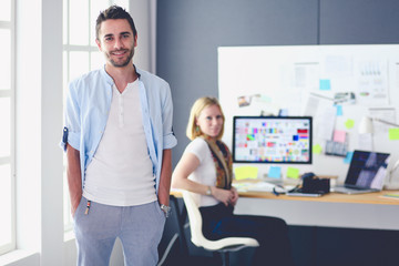 Poster - Portrait of young designer in front of laptop and computer while working. Assistant using her mobile at background.
