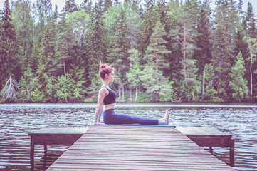 Wall Mural - Young yogi  girl  practicing yoga, sitting in Staff exercise, Dandasana pose on the lake. The concept of appeasement,  healthy lifestyle.