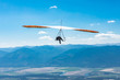 Hang glider man flying in clear sunny day. Flight over Kootenay valley mountains, Creston, British Columbia, Canada. Long shot
