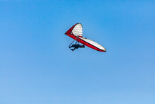 Overhead View Of Flying Hang-gliding Against The Clear Blue Sky. Hang Glider Flying Soaring On A Sunny Day. View From The Bottom