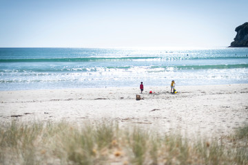 Two children playing on a deserted white sandy beach at low tide on a summer day with a pale blue sky and an island in the distance