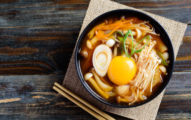 Wall Mural - Kimchi soup with mushroom and egg yolk in a bowl with chopsticks on wooden background, Korean food, top view