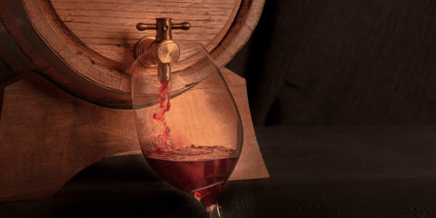 Canvas Print - Pouring wine into a glass from an oak barrel, a toned panorama on a dark background with copy space