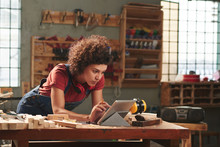 Young Concentrated Woman With Curly Hair Reading Instructions On Digital Tablet Before Working With Wood