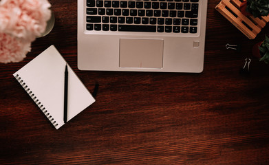 Home office desk workspace with laptop, bouquet of flowers and succulents on a dark background. Flat lay, top view minimal freelancer work concept with copy space mockup.