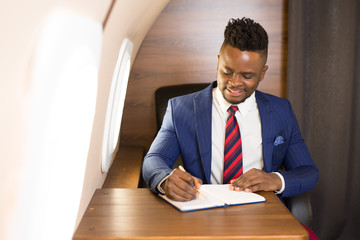 Wall Mural - handsome african young man in suit in private jet cabin with notebook