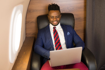 Wall Mural - handsome african young man in suit in private jet cabin with laptop