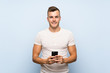 © luismolinero - Young handsome blonde man over isolated blue background using mobile phone