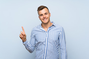 Wall Mural - Young handsome blonde man over isolated blue background showing and lifting a finger in sign of the best