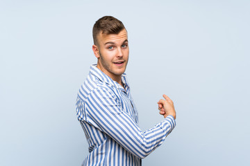 Wall Mural - Young handsome blonde man over isolated blue background pointing back