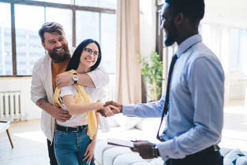 Black realtor greeting cheerful couple in apartment