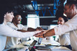 © BullRun - Content multiracial colleagues putting hands together while standing by desk during meeting