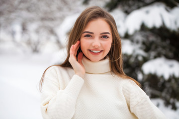 Wall Mural - Young beautiful woman in a woolen sweater posing on a background of a winter park