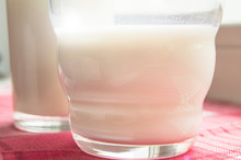 Close-up Of Two Glasses Of Milk On A Checkered Red Napkin, Sunlight, Healthy Food And Diet Drink Concept For Children And Adults