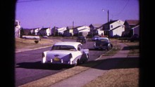 HAGERSTOWN MARYLAND USA-1966: Person In Black Car Takes Off Driving Down The Street Of A Suburban Neighborhood