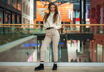 Wall Mural - Portrait of a young beautiful woman in beige sweater and pants posing in the mall