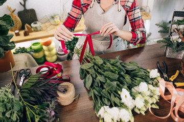 top view on young woman florist hands tying ribbon on wonderful bouquet of flowers lying on wooden table