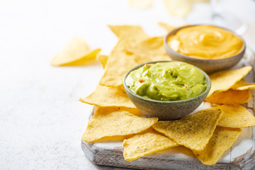 Wall Mural - Nachos chips in a bowl with sauces guacamole and cheese, dip variety, over white stone background.