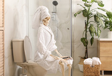 Skeleton In Bathrobe With Mobile Phone Sitting On Toilet Bowl