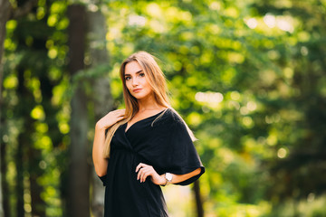 Wall Mural - A young woman in a black dress holds her hand at her waist in th