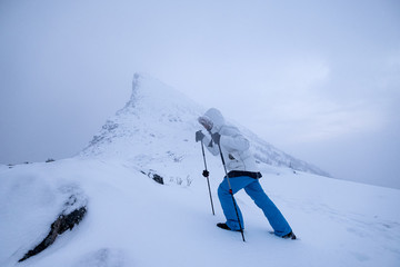 Wall Mural - man climber with trekking poles standing on snow mountain peak in gloomy