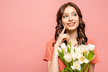 Wall Mural - happy girl looking away and touching cheek while holding bouquet of white tulips isolated on pink