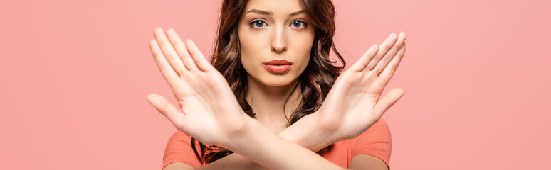 Wall Mural - panoramic shot of serious young woman showing stop gesture while looking at camera isolated on pink