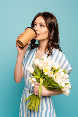 Wall Mural - dreamy young woman drinking coffee to go while holding white tulips isolated on blue