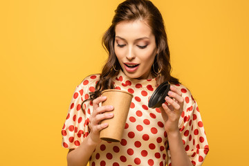 Wall Mural - shocked young woman looking in paper cup isolated on yellow