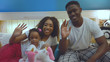 © Fractal Pictures - Funny happiness family moments. Cheerful afro-american ethiopian parents smiling at camera taking selfies in bed.