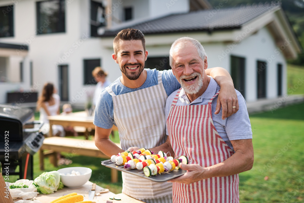 Portrait of father and son outdoors on garden barbecue, grilling. - obrazy, fototapety, plakaty 
