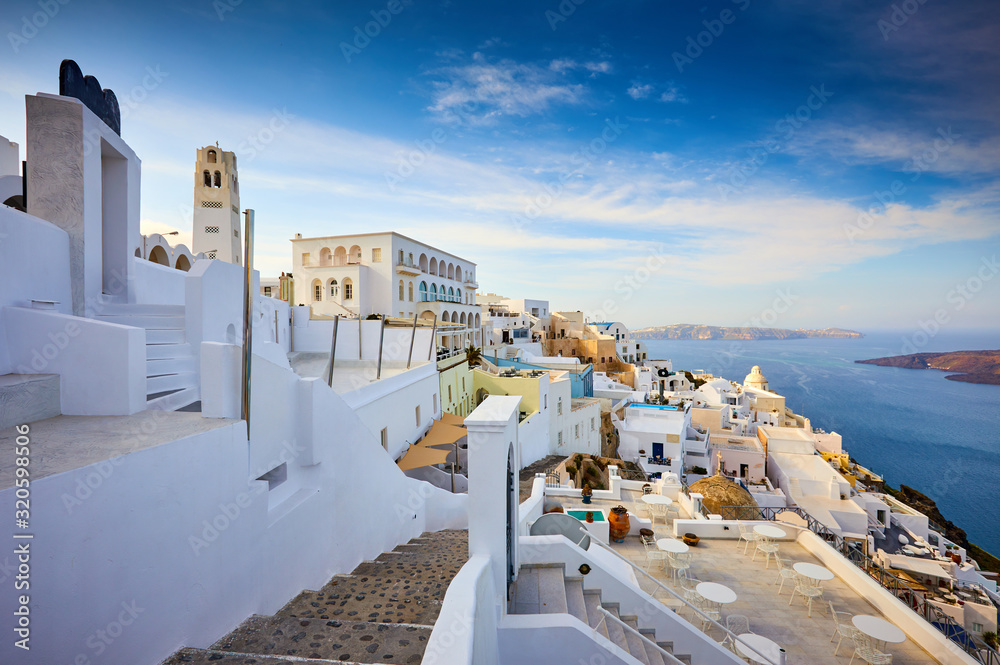Fira town on Santorini island, Greece. Traditional and famous houses and churches with blue domes over the Caldera, Aegean sea. Terraces of Santorini hotels in the morning light. - obrazy, fototapety, plakaty 